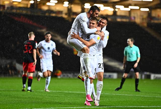 <p>Troy Parrott and Daniel Harvie mob Scott Twine after scoring for MK Dons on Tuesday night. Twine’s hat-trick against Fleetwood Town helped Dons earn a point</p>