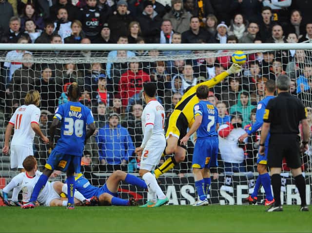<p>Jon Otsemobor watches on as his ‘Heel of God’ flick lofts over Neil Sullivan back in December 2012 when MK Dons beat AFC Wimbledon in the first meeting between the sides</p>
