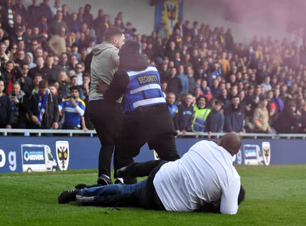 <p>Stewards tackle someone invading the pitch during last season’s heated match between MK Dons and AFC Wimbledon at Plough Lane last season</p>