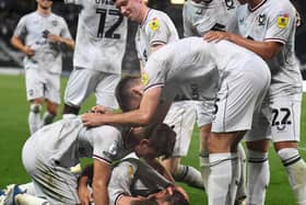 MK Dons pile on to celebrate Bradley Johnson’s winning goal against Port Vale on Tuesday night to secure their first league win of the season, lifting them off the bottom of the table