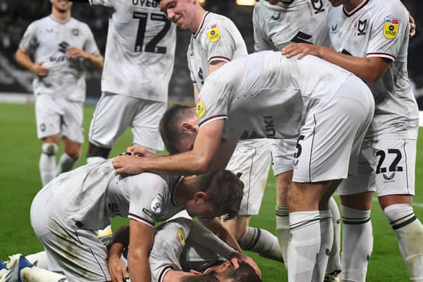 MK Dons pile on to celebrate Bradley Johnson’s winning goal against Port Vale on Tuesday night to secure their first league win of the season, lifting them off the bottom of the table