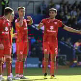 Warren O’Hora and Jack Tucker bark orders at Conor Grant during the 2-1 win over Oxford United on Saturday. Dons’ last eight goals conceded have come from dead ball situations