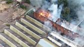 Flames and smoke pour from roof of factory building.