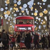 Shoppers cross in front of a London bus as it travels under Christmas lights on Oxford Street in central London in 2017 (Photo: JUSTIN TALLIS/AFP via Getty Images)