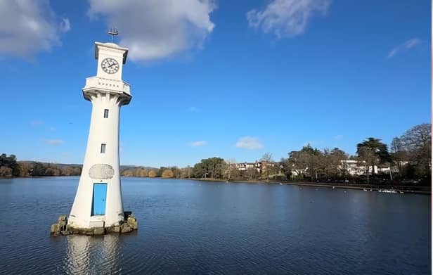 A white clock tower surrounded by water in a serene location
