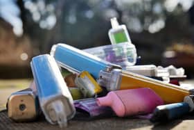 Discarded electronic cigarette vapes that have been collected from roads and pavements shot over a pale concrete slab background