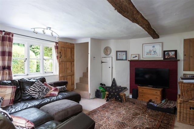 The sitting room has exposed ceiling beams and wall timbers with a window seat and fireplace with cast iron log burning stove