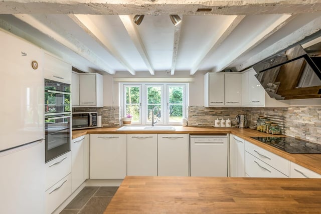 The country-contemporary style kitchen features white gloss units, wooden worktops, ceramic sink, and stone splashbacks with utility and cloakroom behind a sliding door.