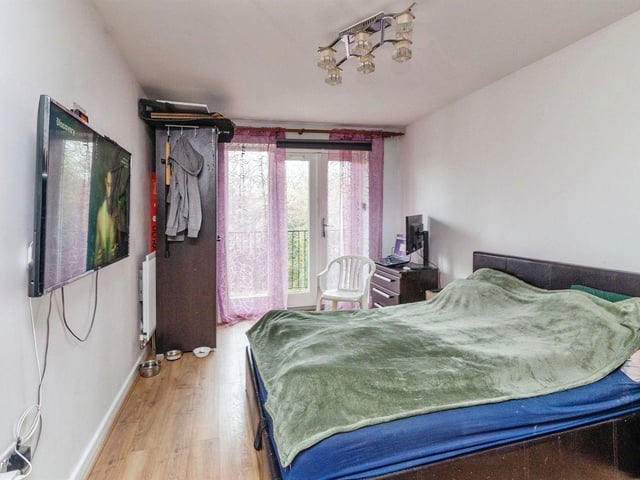 The front bedroom has laminated flooring, a double glazed patio door leading to balcony, and a wall mounted radiator.
