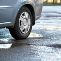 Close up of car wheel on a road in very bad condition with big potholes full of dirty rain water pools.
