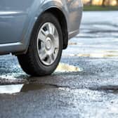 Close up of car wheel on a road in very bad condition with big potholes full of dirty rain water pools.
