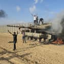 Palestinians celebrate by a destroyed Israeli tank at the Gaza Strip fence east of Khan Younis Saturday, Oct. 7, 2023. The militant Hamas rulers of the Gaza Strip carried out an unprecedented, multi-front attack on Israel at daybreak Saturday, firing thousands of rockets as dozens of Hamas fighters infiltrated the heavily fortified border in several locations by air, land, and sea and catching the country off-guard on a major holiday (AP Photo/Hassan Eslaiah)