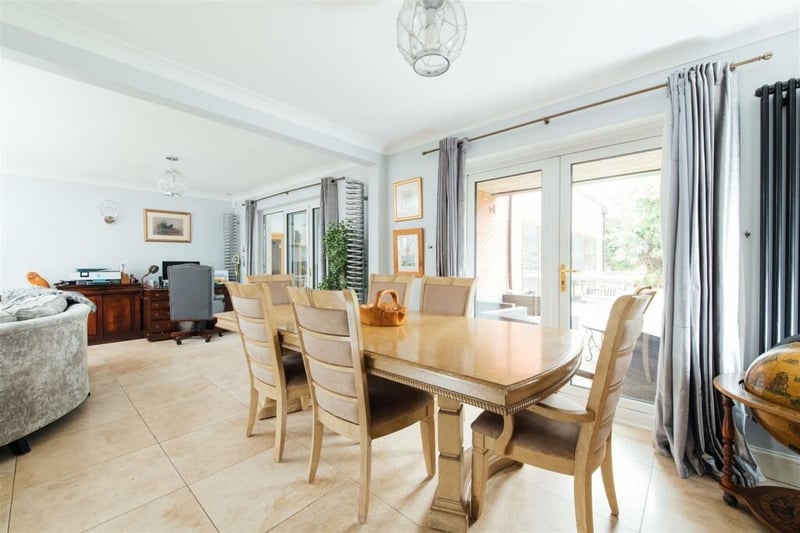 An L shape lounge and dining room has a tiled floor. The dining area has French doors opening to the rear garden and the living room area has a fireplace with stone surround and hearth.