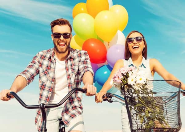 Low angle view of cheerful young couple smiling and riding on bicycles with colorful balloons in the background